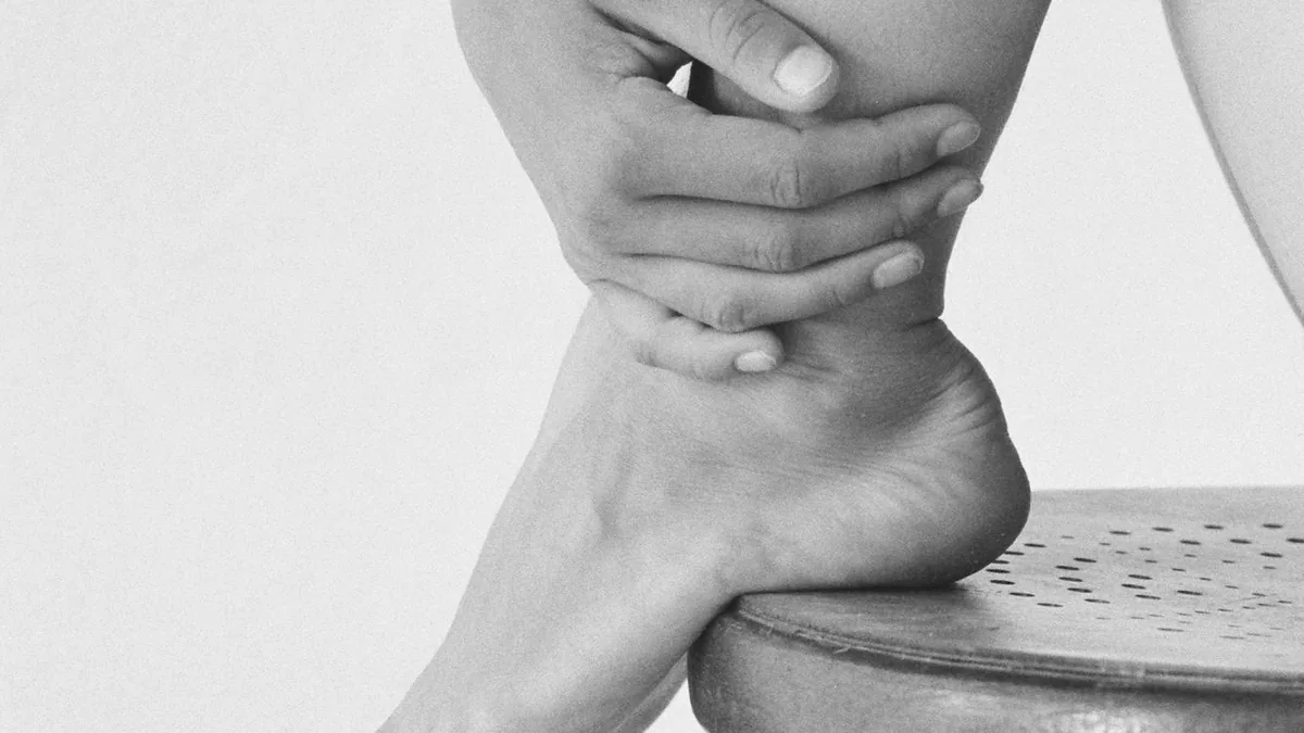 Monochrome image capturing the elegance of a woman's feet and hands on a stool.