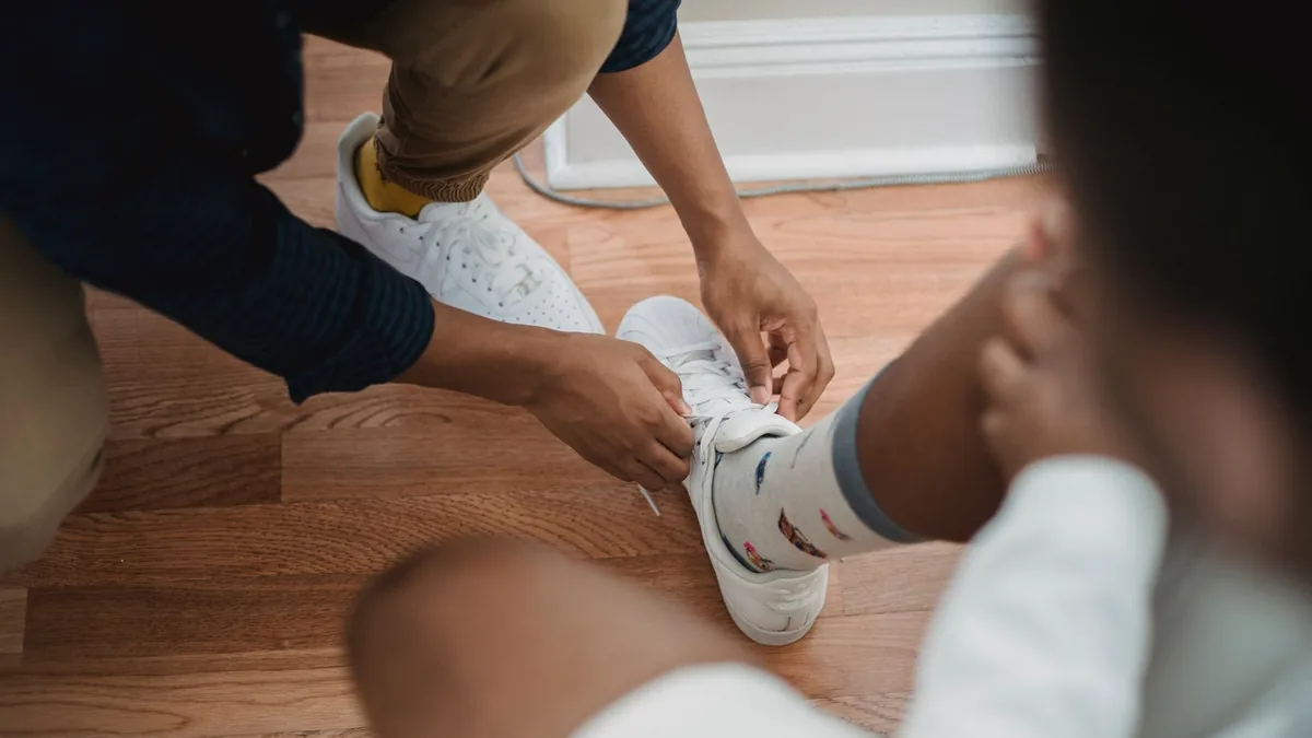 Close-up of a person tying sneakers with colorful socks on a wooden floor.