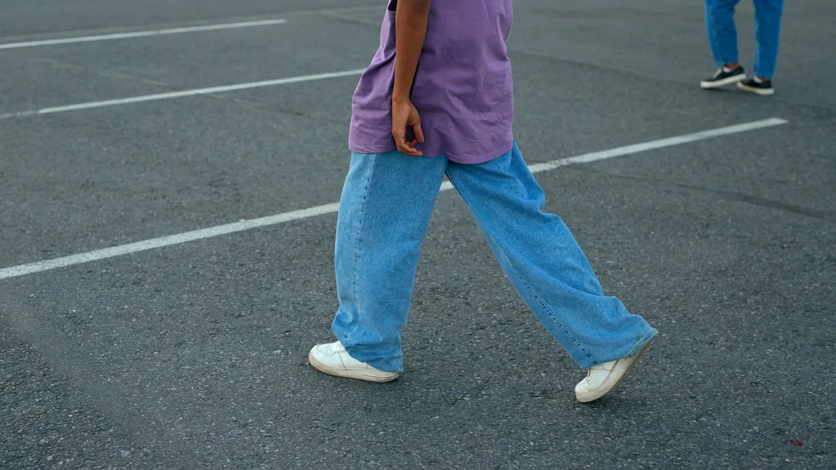 Unrecognizable person walking in a parking lot wearing a purple top and denim jeans.