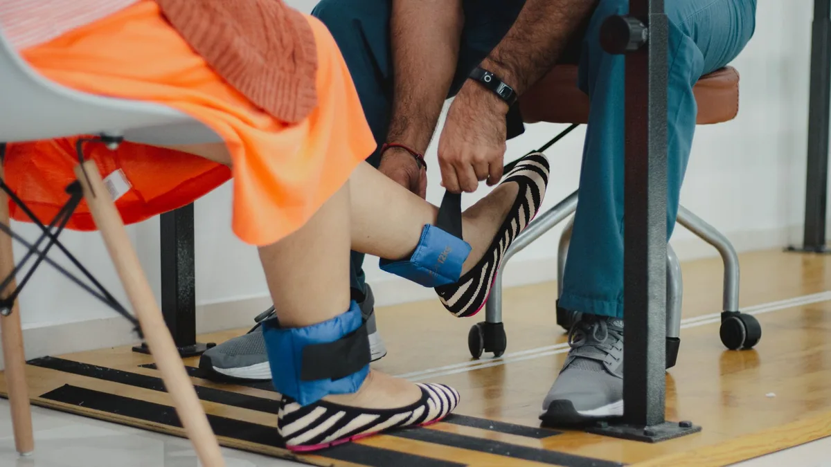 A therapist assists a woman during a rehabilitation session involving ankle weights.