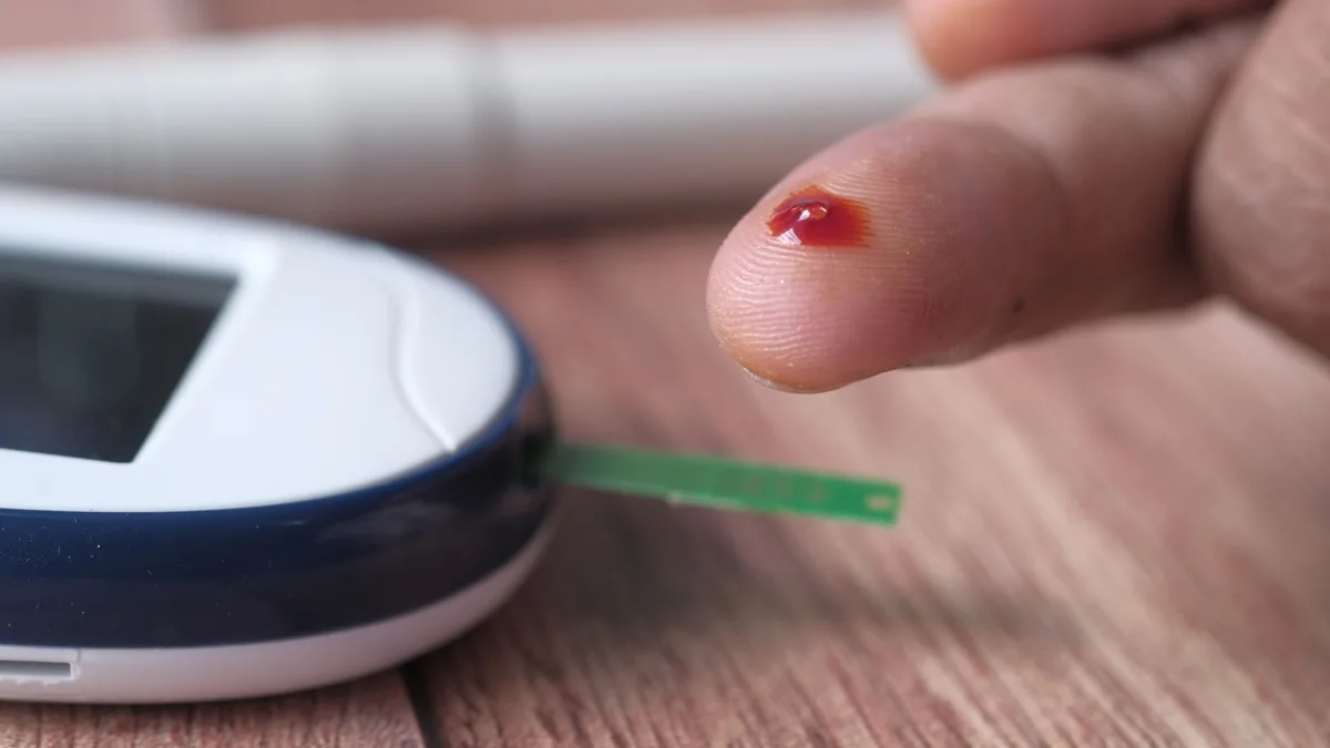 A close-up of a finger prick and blood glucose monitor for diabetes testing.
