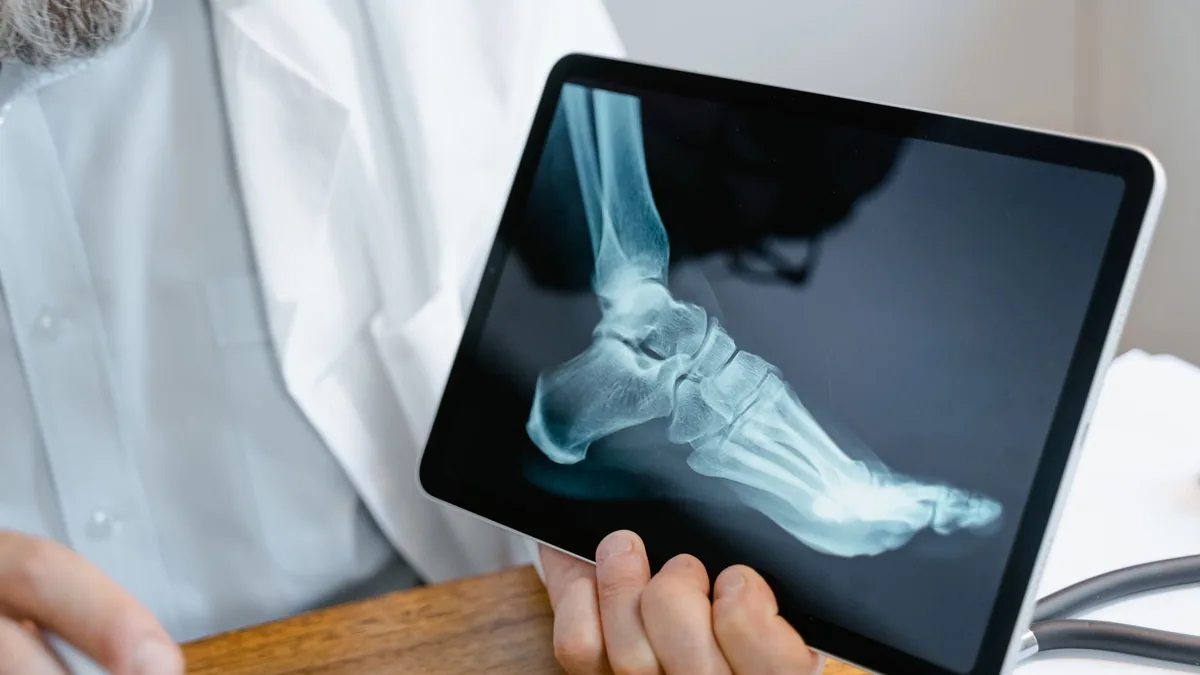 A doctor examines an x-ray image of a foot displayed on a tablet.
