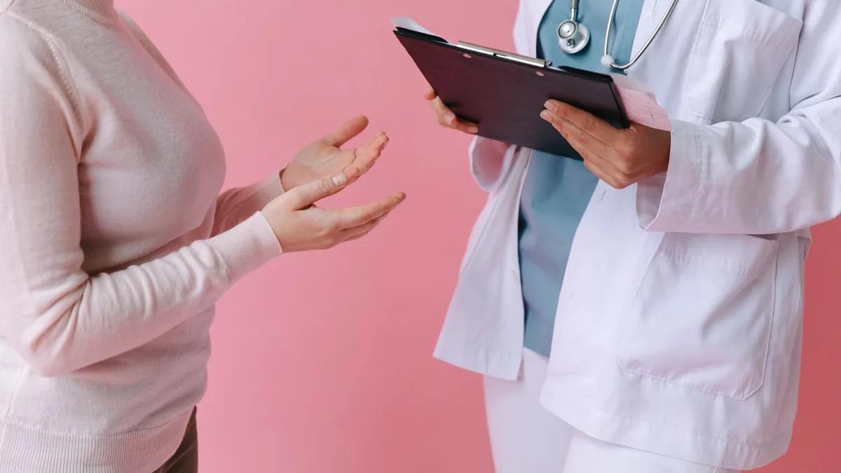 Close-up of a patient consulting a doctor with a clipboard in a medical setting.