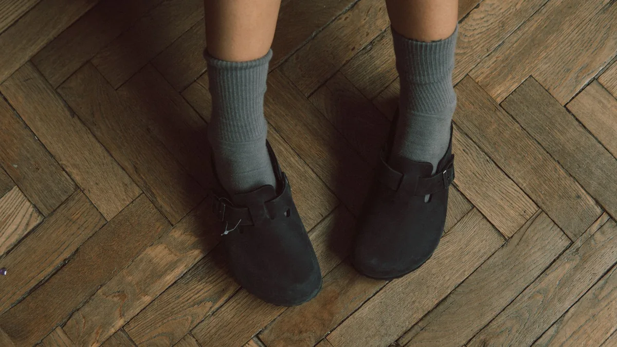 Close-up of a person wearing black sandals with blue socks on a wooden parquet floor.