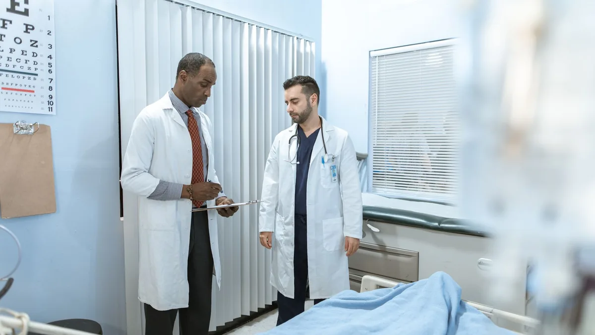 Two doctors review a patient's chart in a hospital room, focusing on healthcare cooperation and medical care.