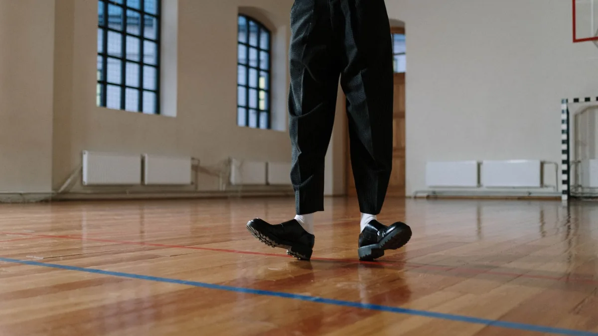 Fashionable black leather shoes and black pants on a polished gym floor creating a modern vibe.