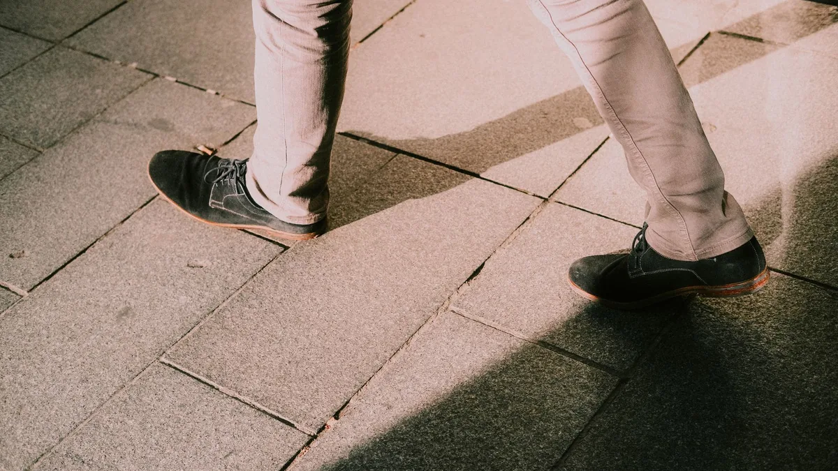Close-up of legs in black shoes walking on stone pavement with shadows.