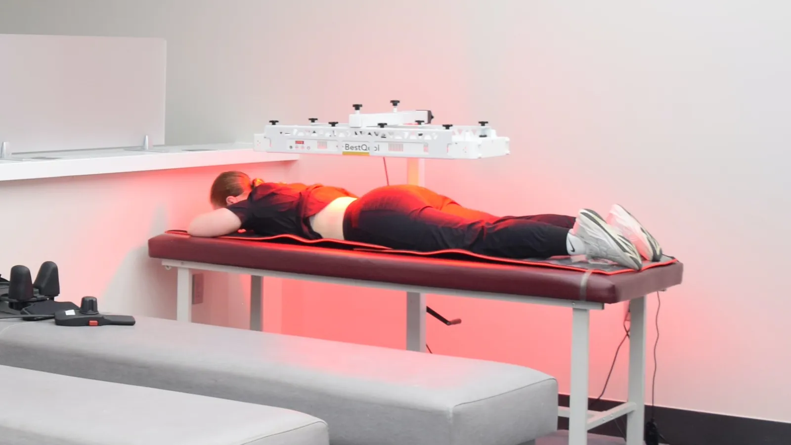 Patient lying face down under a red-light photobiomodulation panel on a treatment table at Regenerve, 4477 Woodson Rd, St. Louis, MO 63134